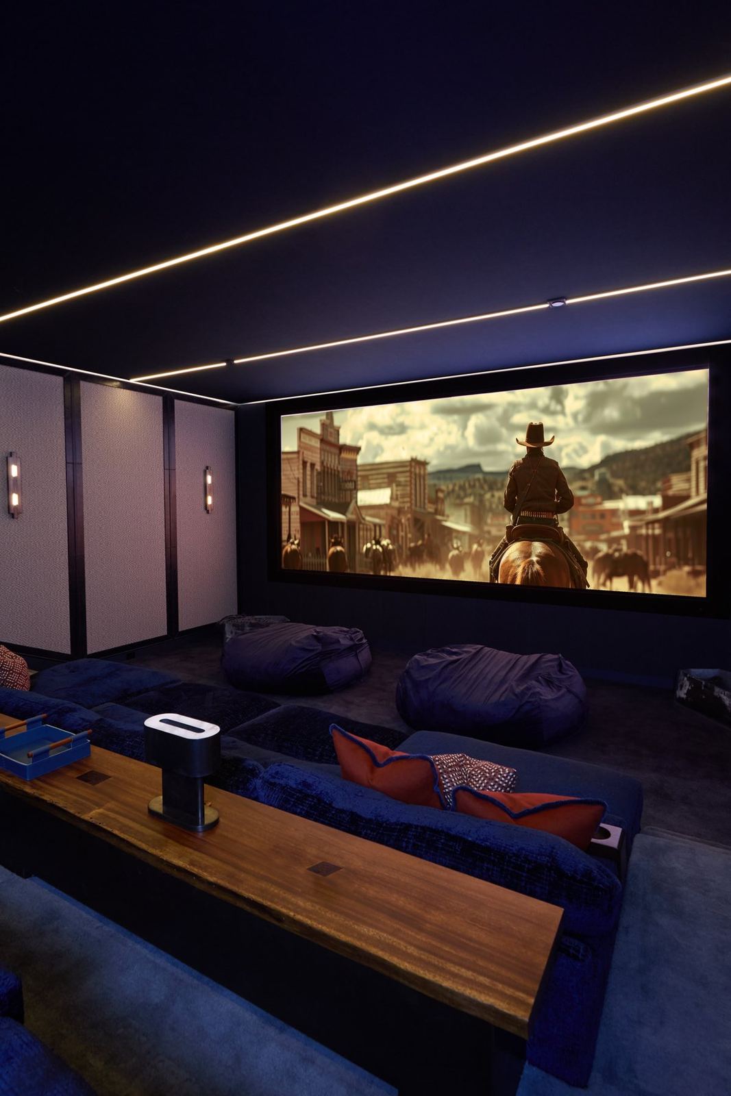 The finished private cinema — fabric walls, linear ceiling light, lounge seating, and a cinemascope screen
